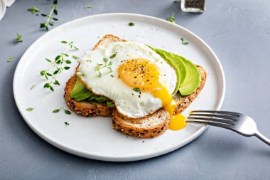 Avocado toast on a toasted multigrain bread with a fried egg on top and running yolk