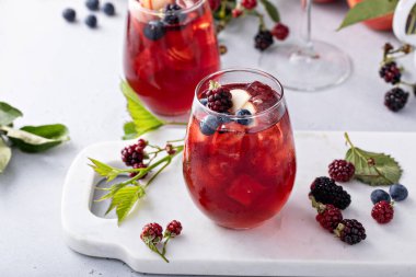 Fall berry and apple sangria in a glass with ice, refreshing fall cocktail or mocktail idea