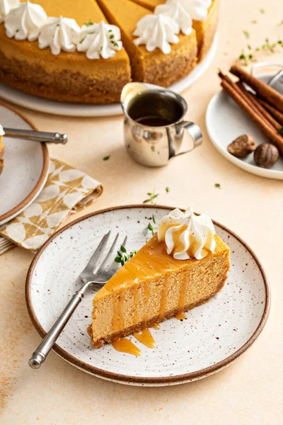 Pumpkin cheesecake with fall spices topped with whipped cream, dessert for Thanksgiving, a slice cut with caramel sauce
