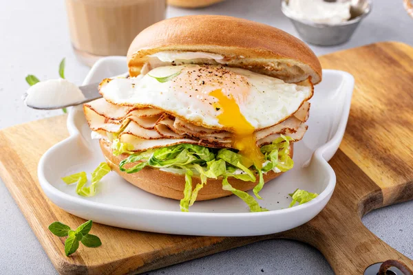 Turkey bagel breakfast sandwich with cream cheese, lettuce and fried egg with runny yolk