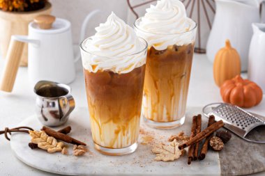 Iced pumpkin spice latte in tall glasses topped with whipped cream and caramel sauce