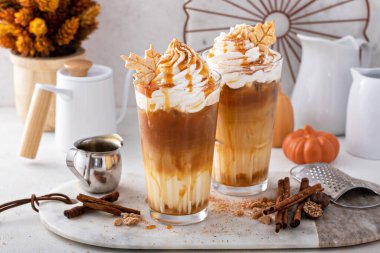 Iced pumpkin spice latte in tall glasses topped with whipped cream and caramel sauce, refreshing and festive fall drink