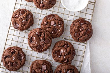 Double chocolate cookies with dark chocolate chips and salt flakes on a cooling rack