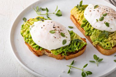 Avocado toast with a perfect poached egg on top with salt and pepper served with coffee for breakfast