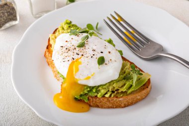 Avocado toast with a perfect poached egg on top with salt and pepper served with coffee for breakfast with runny yolk