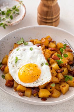 Potato, onion and ham hash for breakfast topped with fried egg