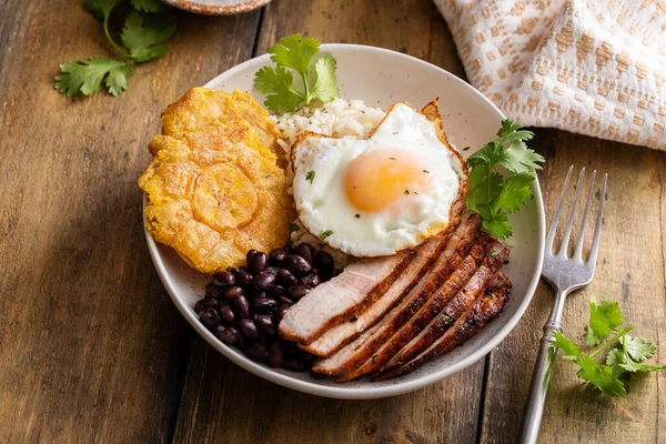 Caribbean or latin american breakfast with rice, beans, tostones and sliced pork topped with fried egg