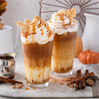 Iced pumpkin spice latte in tall glasses topped with whipped cream and caramel sauce, refreshing and festive fall drink