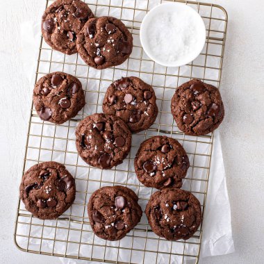 Double chocolate cookies with dark chocolate chips and salt flakes on a cooling rack