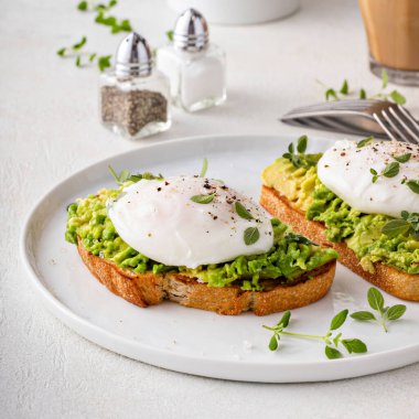 Avocado toast with a perfect poached egg on top with salt and pepper served with coffee for breakfast