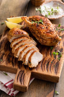 Roasted or seared chicken breast sliced on a cutting board with herbs and spices
