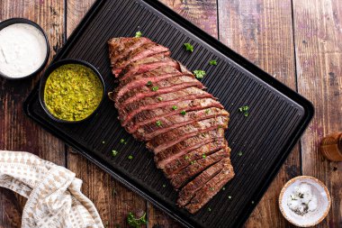Seared flank steak sliced on a grill pan with chimichurri and horseradish sauces