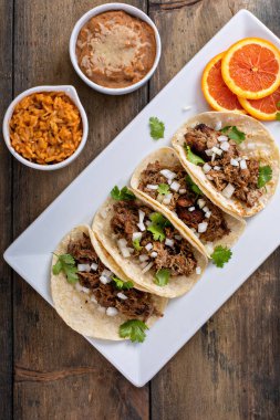 Pork carnitas tacos on corn tortillas served with rice and beans
