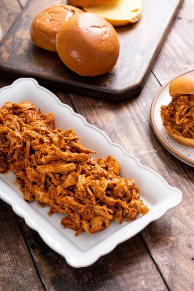 Pulled bbq chicken on a serving plate with brioche buns ready to making sandwiches