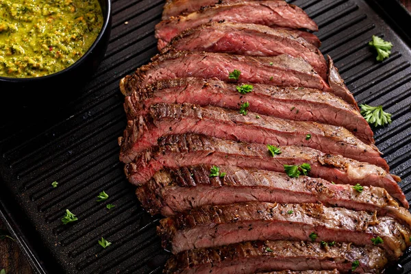 Seared flank steak sliced on a grill pan with chimichurri and horseradish sauces