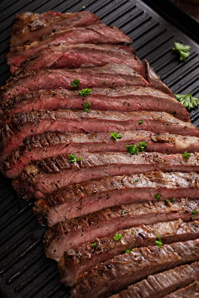 Seared flank steak sliced on a grill pan with chimichurri and horseradish sauces