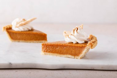 Pumpkin pie slices topped with whipped cream on a marble board, minimalistic look