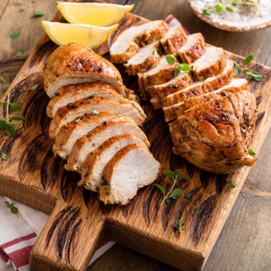 Roasted or seared chicken breast sliced on a cutting board with herbs and spices