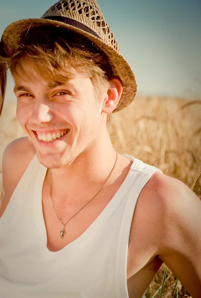 Photo of a young man in a traditional rural hat sitting against wheat field background — Stock Photo, Image