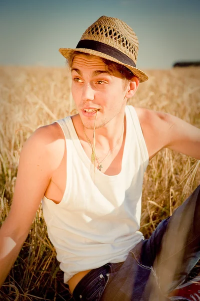 Foto de un joven con un sombrero rural tradicional sentado sobre el fondo del campo de trigo —  Fotos de Stock