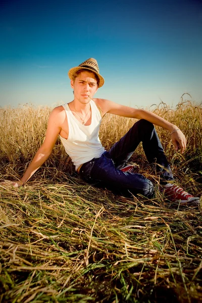 Foto di un giovane uomo in un tradizionale cappello rurale seduto sullo sfondo del campo di grano — Foto Stock