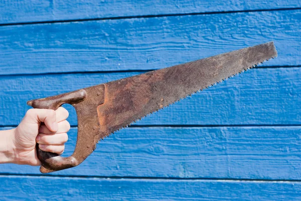 Hand with saw on blue wooden background — Stock Photo, Image