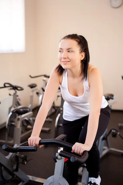 Genç kadın bir eğitim tesisi egzersiz bisikleti — Stok fotoğraf