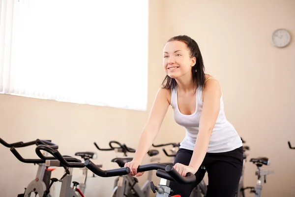 Mujer joven montando una bicicleta de ejercicios de entrenamiento — Foto de Stock
