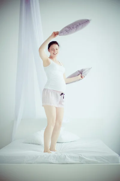 Mladá těhotná žena se házet polštáře v ložnici — Stock fotografie