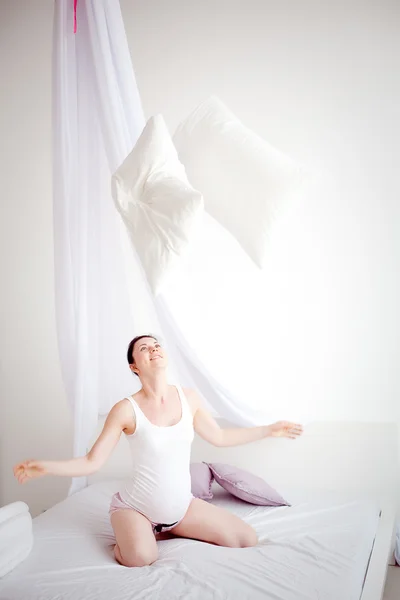 Young pregnant woman are throwing pillows in the bedroom — Stock Photo, Image