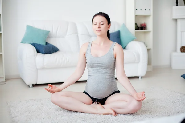 Junge schwangere Frau macht Yoga im Haus Stockbild