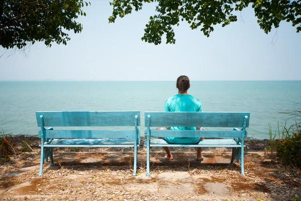 Junger Mann sitzt auf Bank mit Blick aufs Meer — Stockfoto