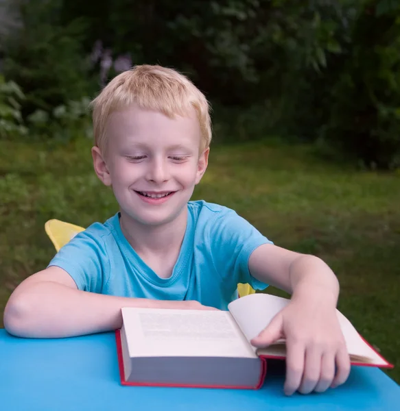 6 - årig pojke läser bok och ler — Stockfoto