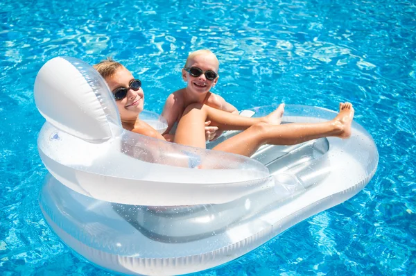 Twee jongens plezier spelen op een zwevende matras in een zwembad — Stockfoto