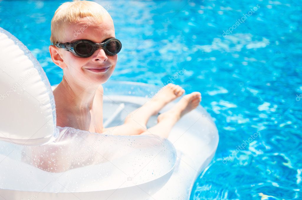 Young smiling boy laying on a floating mattress in a swimming po
