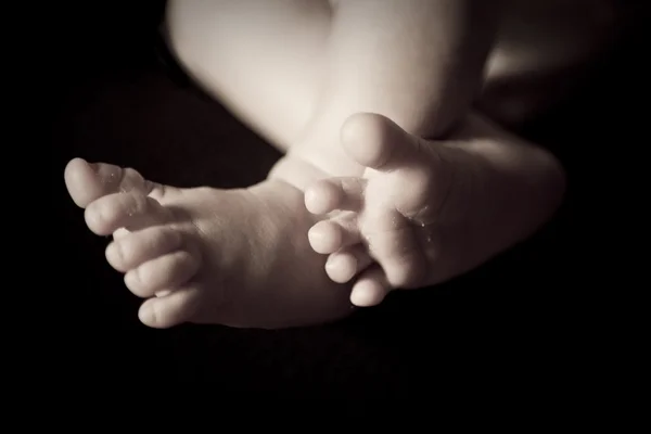 黒の背景に生まれたばかりの赤ちゃんの足 — ストック写真