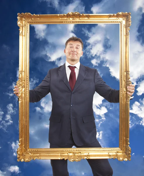 Portret van zakenman houden een gouden frame op blauwe hemel met wolken — Stockfoto