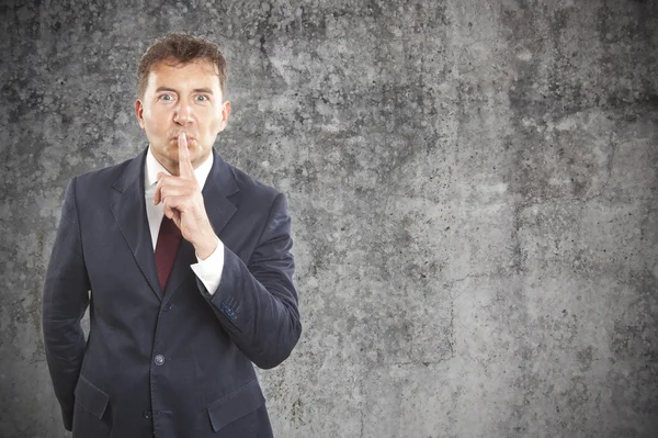 Businessman making silence gesture on cement background — Stock Photo, Image