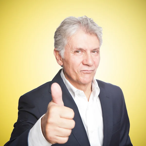 Portrait of confident mature businessman with thumbs up on yellow background — Stock Photo, Image