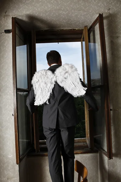 Бизнесмен с ангельскими крыльями смотрит в окно — стоковое фото