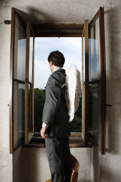 Businessman with angel wings looking through window — Stock Photo, Image