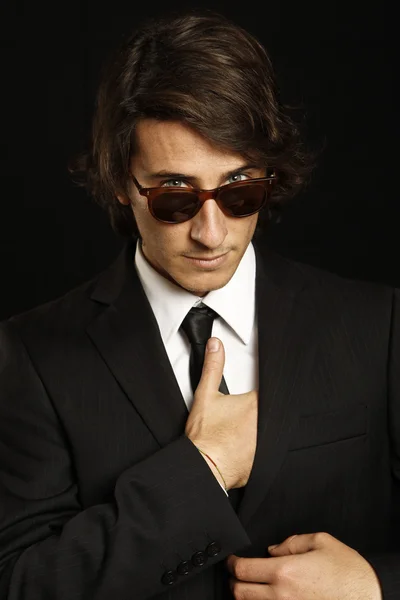 Attractive young man wearing elegant black suit and sunglasses — Stock Photo, Image