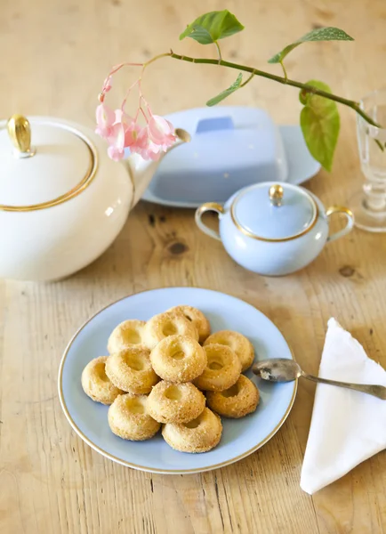 Een bord koekjes, een theepot en een bloem op houten tafel — Stockfoto