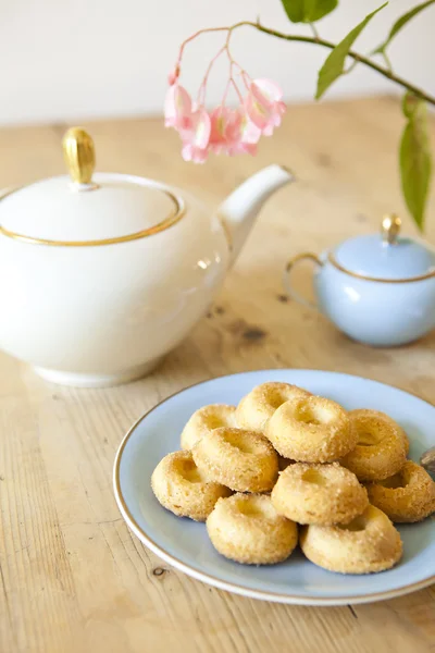 Een bord koekjes, een theepot en een bloem op houten tafel — Stockfoto