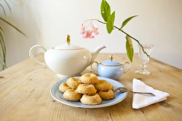 Um prato de biscoitos, um pote de chá e uma flor na mesa de madeira — Fotografia de Stock