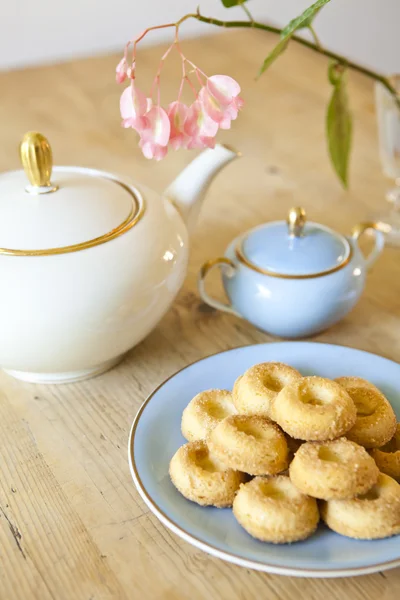 Een bord koekjes, een theepot en een bloem op houten tafel — Stockfoto