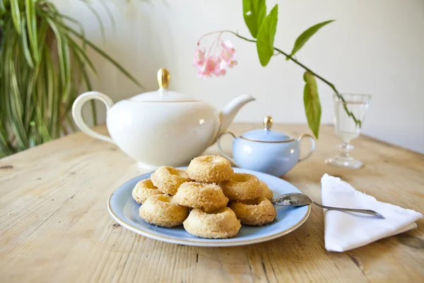 Um prato de biscoitos, um pote de chá e uma flor na mesa de madeira — Fotografia de Stock