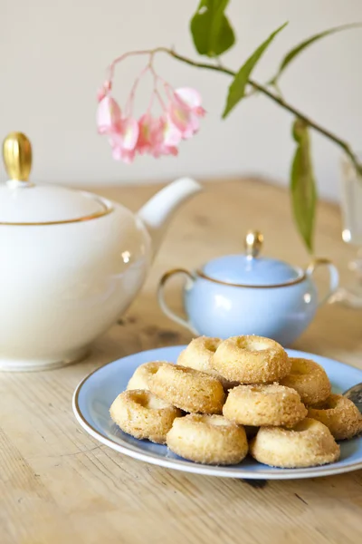 Um prato de biscoitos, um pote de chá e uma flor na mesa de madeira — Fotografia de Stock