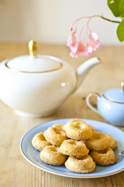 Een bord koekjes, een theepot en een bloem op houten tafel — Stockfoto