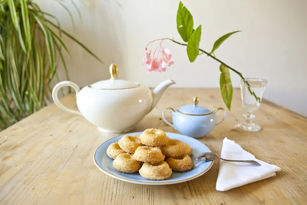 Een bord koekjes, een theepot en een bloem op houten tafel — Stockfoto